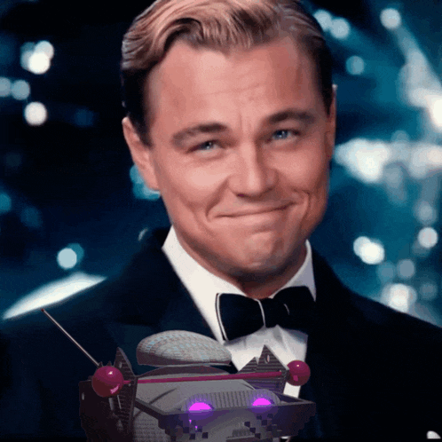 a man in a tuxedo and bow tie is smiling with a robot in the background