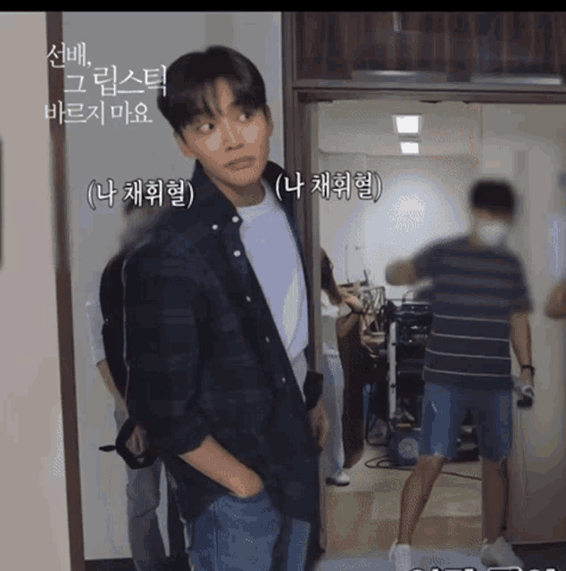 a man in a plaid shirt is standing in a doorway with his hands in his pockets and a foreign language written above him