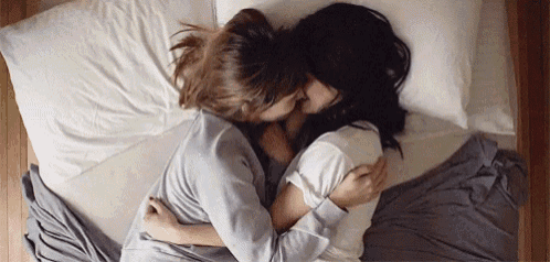 two women are hugging each other while laying in bed .