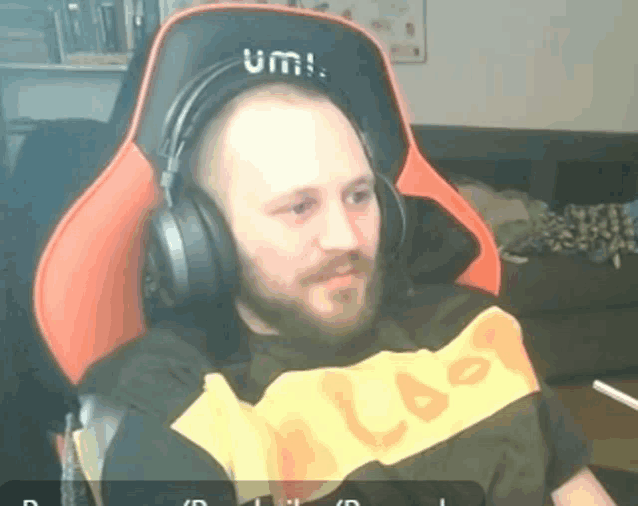 a man wearing headphones and a shirt that says " last " sits in an orange chair