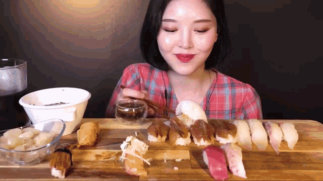 a woman is eating sushi with chopsticks on a wooden cutting board