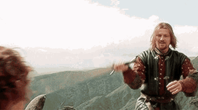 a man is holding a sword while standing on top of a mountain .