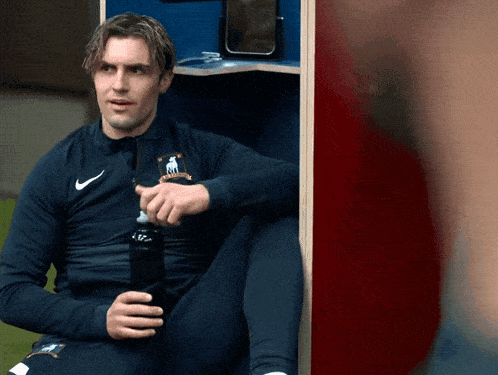 a man in a nike jacket sits in a locker holding a bottle