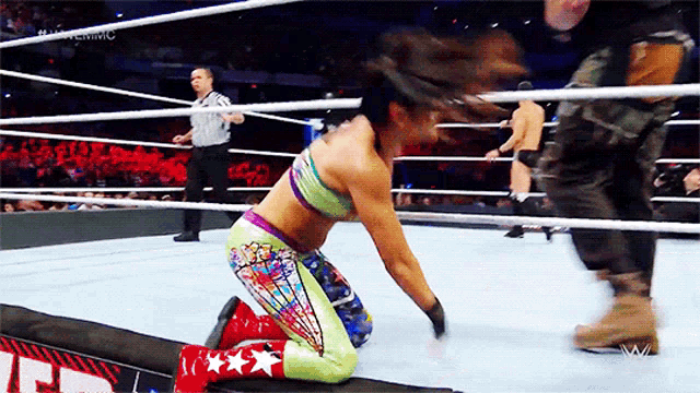 a woman is kneeling down in a wrestling ring with a referee watching