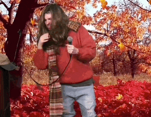 a man in a red jacket is singing into a microphone in a field of leaves .