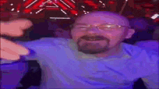 a man with a beard and glasses is sitting in front of a crowd .