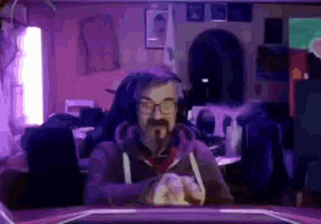 a man with glasses and a beard is sitting in a chair in a dark room