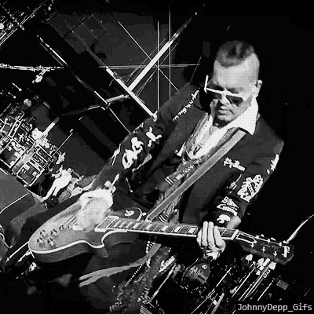 a man in a suit and sunglasses is playing a guitar on a stage .