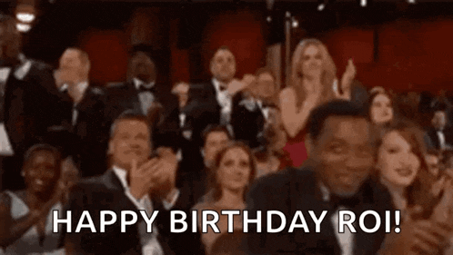 a group of people are sitting in a theatre applauding and saying happy birthday roi .