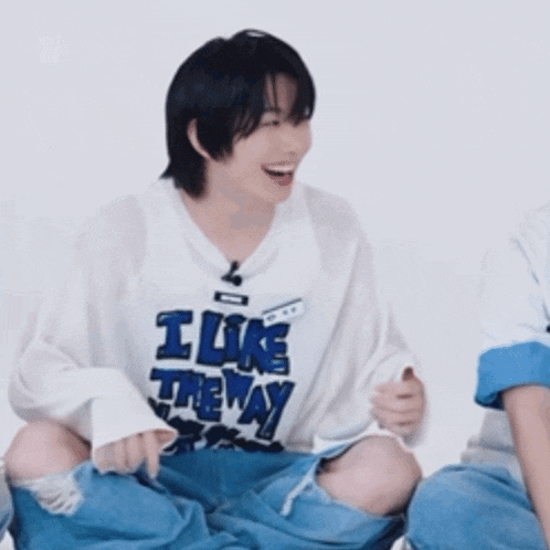 a young man wearing a white shirt that says i like the way is laughing .