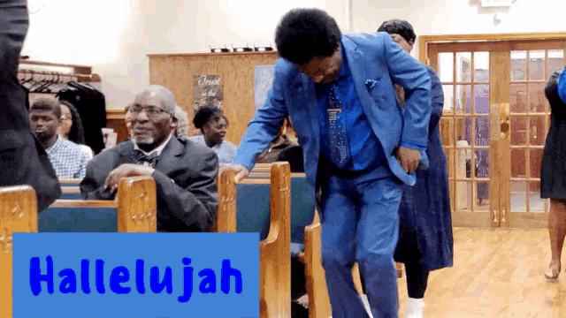 a man in a blue suit is dancing in a church with a sign that says hallelujah on it