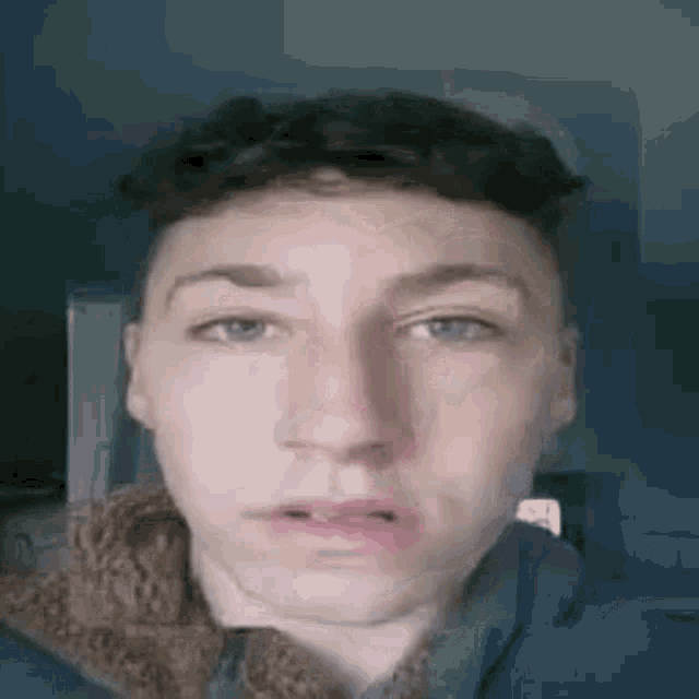 a young man in a blue jacket is making a funny face with his mouth open .