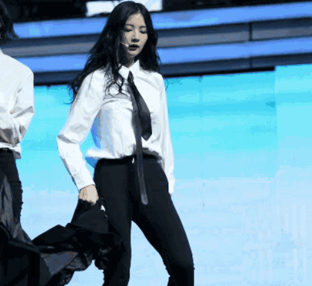 a woman in a white shirt and black tie is standing on a stage