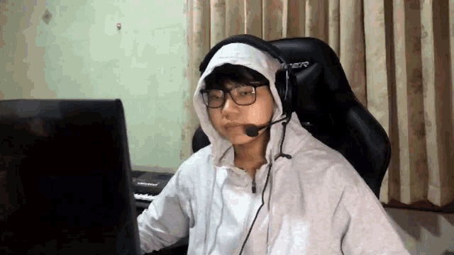 a person wearing headphones and a hoodie is sitting in front of a computer .