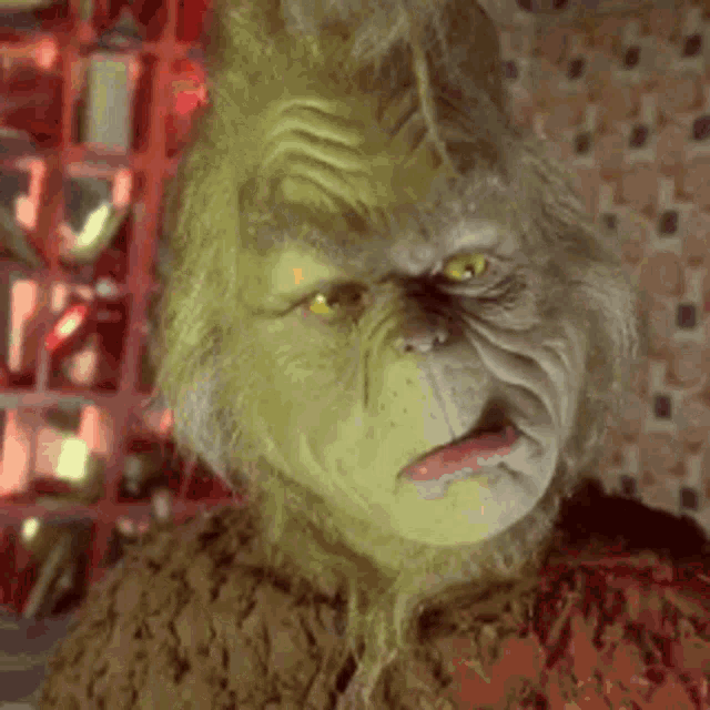 a close up of a grinch 's face in a room with a shelf in the background .
