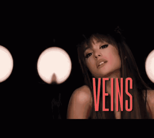 ariana grande is making a funny face in a dark room with lights behind her .