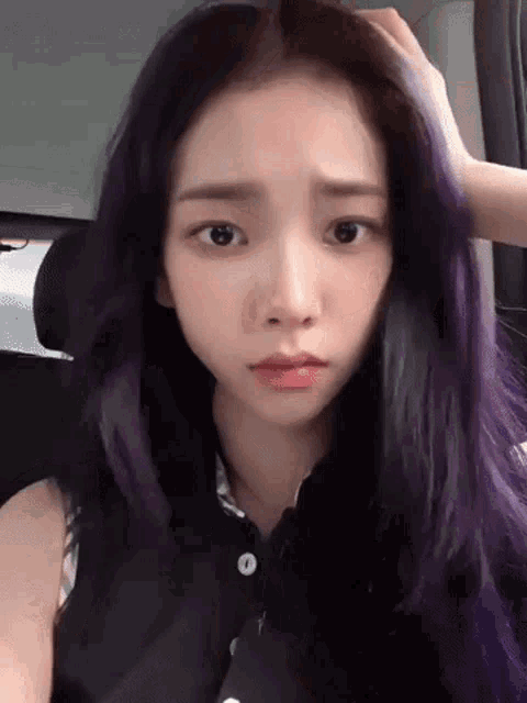 a young woman with purple hair is sitting in a car and touching her hair .