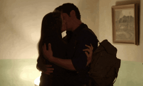 a man and woman kissing in front of a framed painting