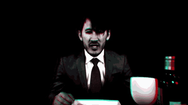 a man in a suit and tie is sitting at a table with a glass of wine in front of him .
