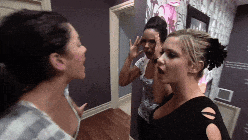 three women are standing next to each other in a room with a purple wall