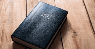 a black holy bible is sitting on a wooden table .