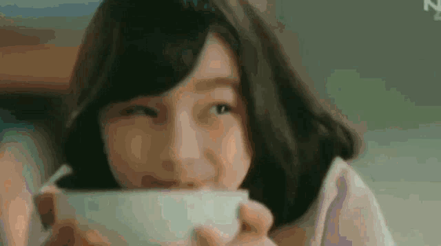 a woman is drinking from a white cup and looking at the camera .