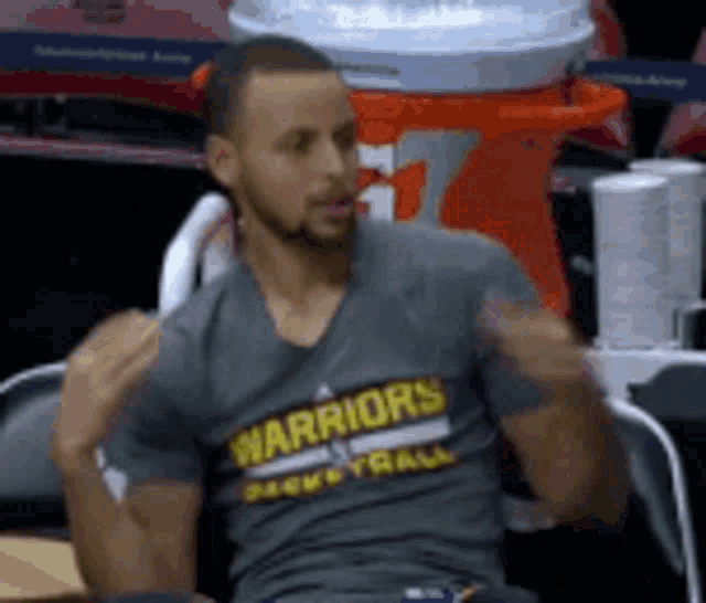 a man wearing a warriors basketball shirt is sitting in a chair