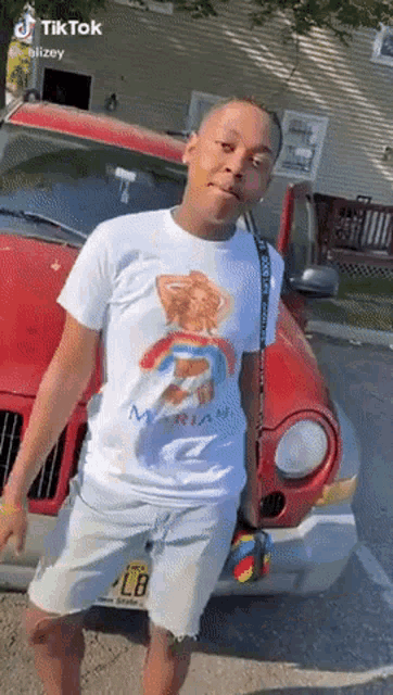 a young man wearing a t-shirt with a rainbow on it is standing in front of a red car .