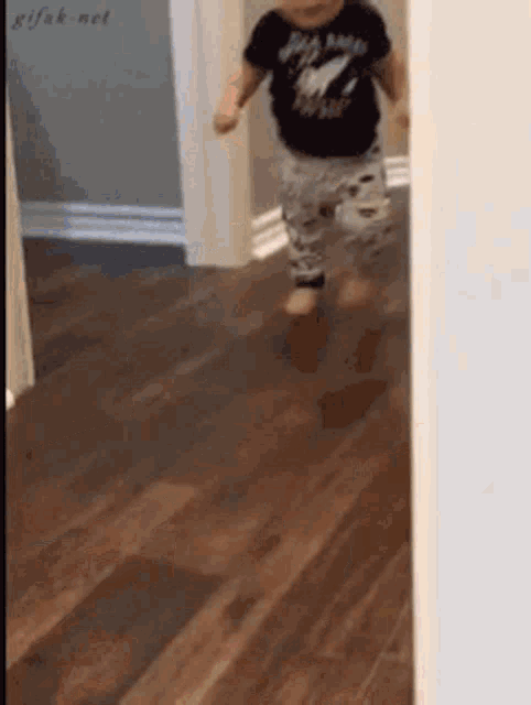 a baby wearing a black shirt that says ' rolling stones ' on it is running on a wooden floor