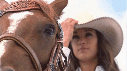 a woman in a cowboy hat adjusts the bridle on her horse