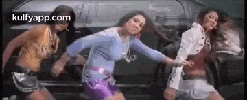 three women are dancing in front of a car in a movie .