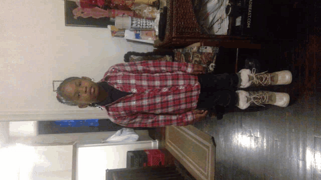 a young boy wearing a plaid shirt and white boots stands in front of a sign that says ' breast.com '