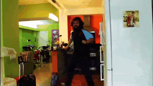 a man with a beard is dancing in front of a refrigerator with a picture of a man on it