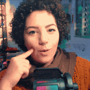 a woman with curly hair and a nose ring holds her finger to her mouth