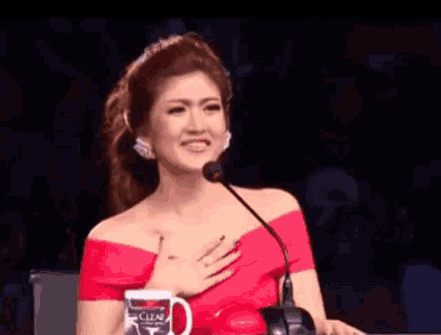 a woman in a red off the shoulder top is sitting in front of a microphone