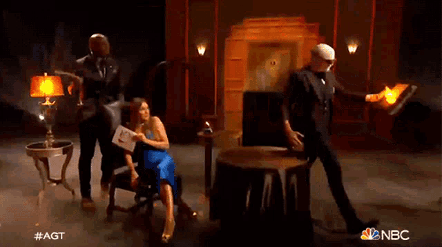 a woman sits in a chair next to a man holding a fire torch and a sign that says #agt