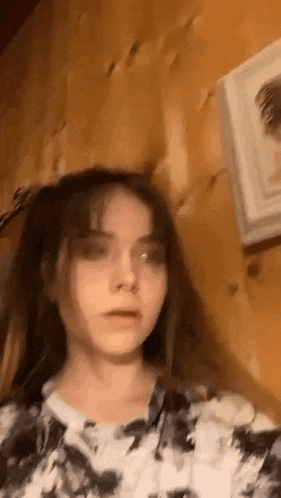 a girl with long hair is standing in front of a wooden wall and looking at the camera .