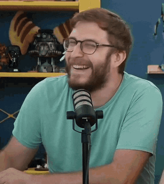 a man with glasses and a beard is laughing in front of a microphone that says pop