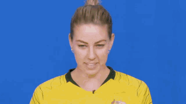 a woman in a yellow shirt is pointing up with her finger against a blue background .
