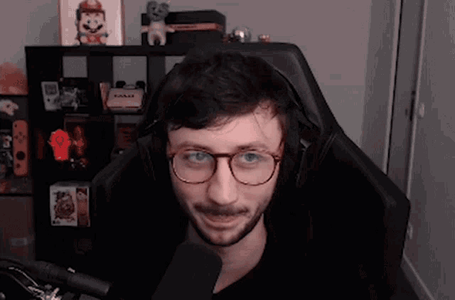 a man wearing glasses and headphones is sitting in a chair in front of a microphone .