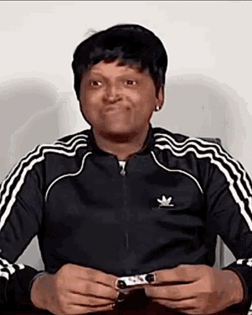 a man in a black adidas jacket is making a funny face while holding a ring .