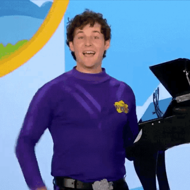 a man in a purple wiggle shirt is holding a black piano