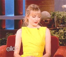 a woman in a yellow dress sits on a red couch in front of an ellen show