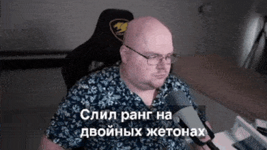 a man wearing glasses and a blue shirt is sitting in front of a microphone with a foreign language caption