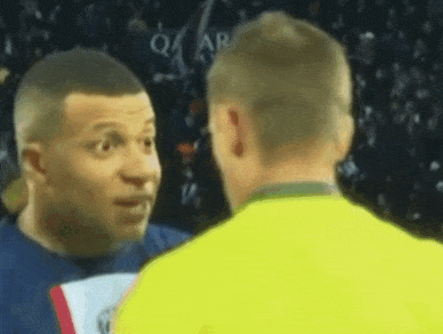 a man in a yellow shirt is talking to another man in a blue shirt on a soccer field .