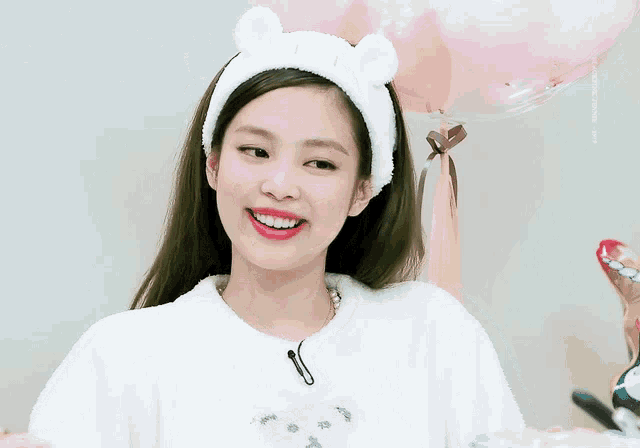 a woman wearing a headband with bunny ears is smiling in front of balloons .
