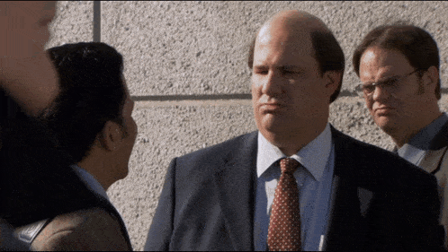 a bald man in a suit and tie stands in a crowd