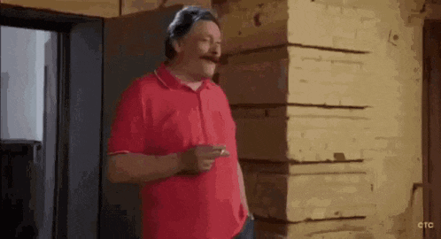 a man in a red shirt is smoking a cigarette in front of a wooden wall .