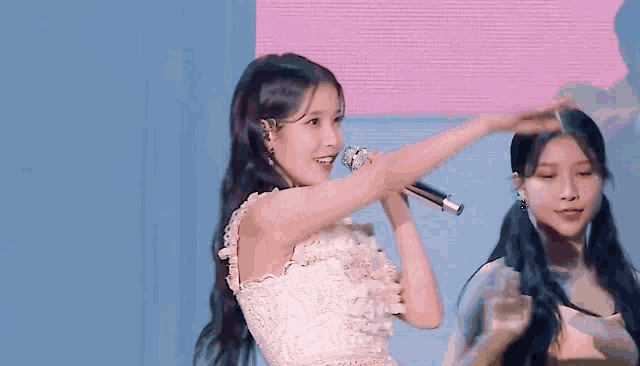 a woman in a white dress is singing into a microphone while another woman stands behind her .