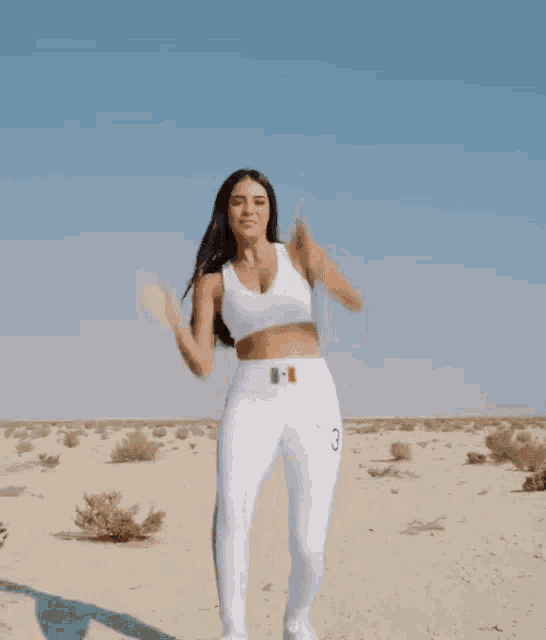 a woman in a white crop top and white pants is dancing in the desert